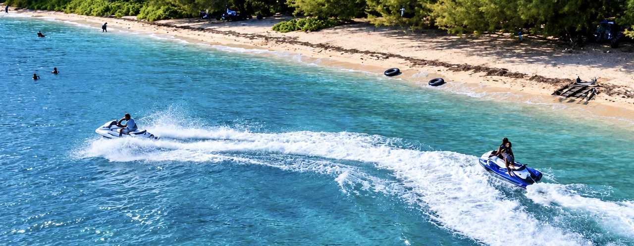 Two jet skis carving curved wakes beside a sandy shoreline, viewed from above.